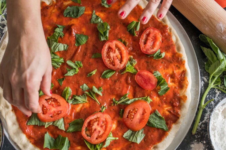 Looking down on hands building a pizza with fresh tomatoes and basil leaves in a Seattle area cooking classes