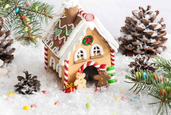 A homemade gingerbread house covered with candy on a bed of snow and surrounded by pinecones