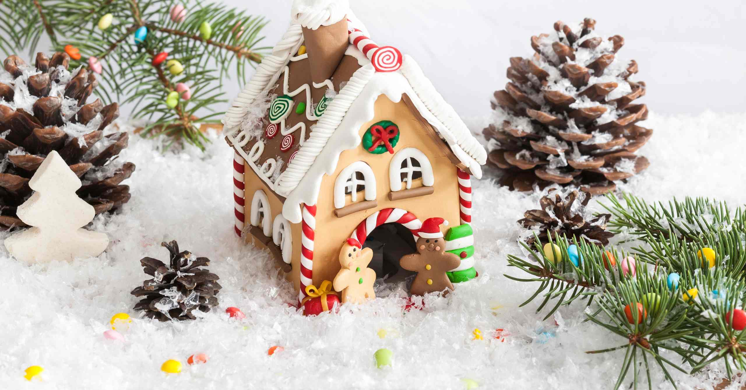 A homemade gingerbread house covered with candy on a bed of snow and surrounded by pinecones